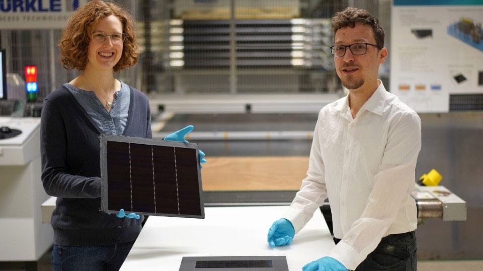 Project manager Dr Laura Stevens shows one of the III-V germanium PV modules with a record efficiency of 34.2%. Leonhard Böck is a member of the project team and played a key role in developing the III-V silicon PV module with 31.3% efficiency that lies in front of him. (© Fraunhofer ISE/photo: Jacob Forster.) 